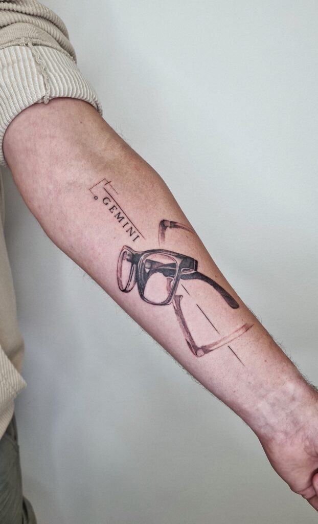 Minimalist glasses and Gemini zodiac tattoo on the forearm — Gruntins Tattoo, Liepāja