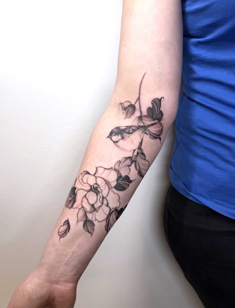 Black and grey bird and flowers tattoo on the forearm